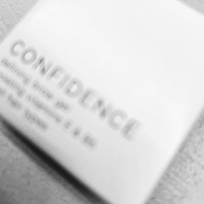 Ein verschwommenes Bild der Produktverpackung vom Confidence Defining Brow Gel. Das Foto ist schwarz-weiß und dient als Stilmittel.